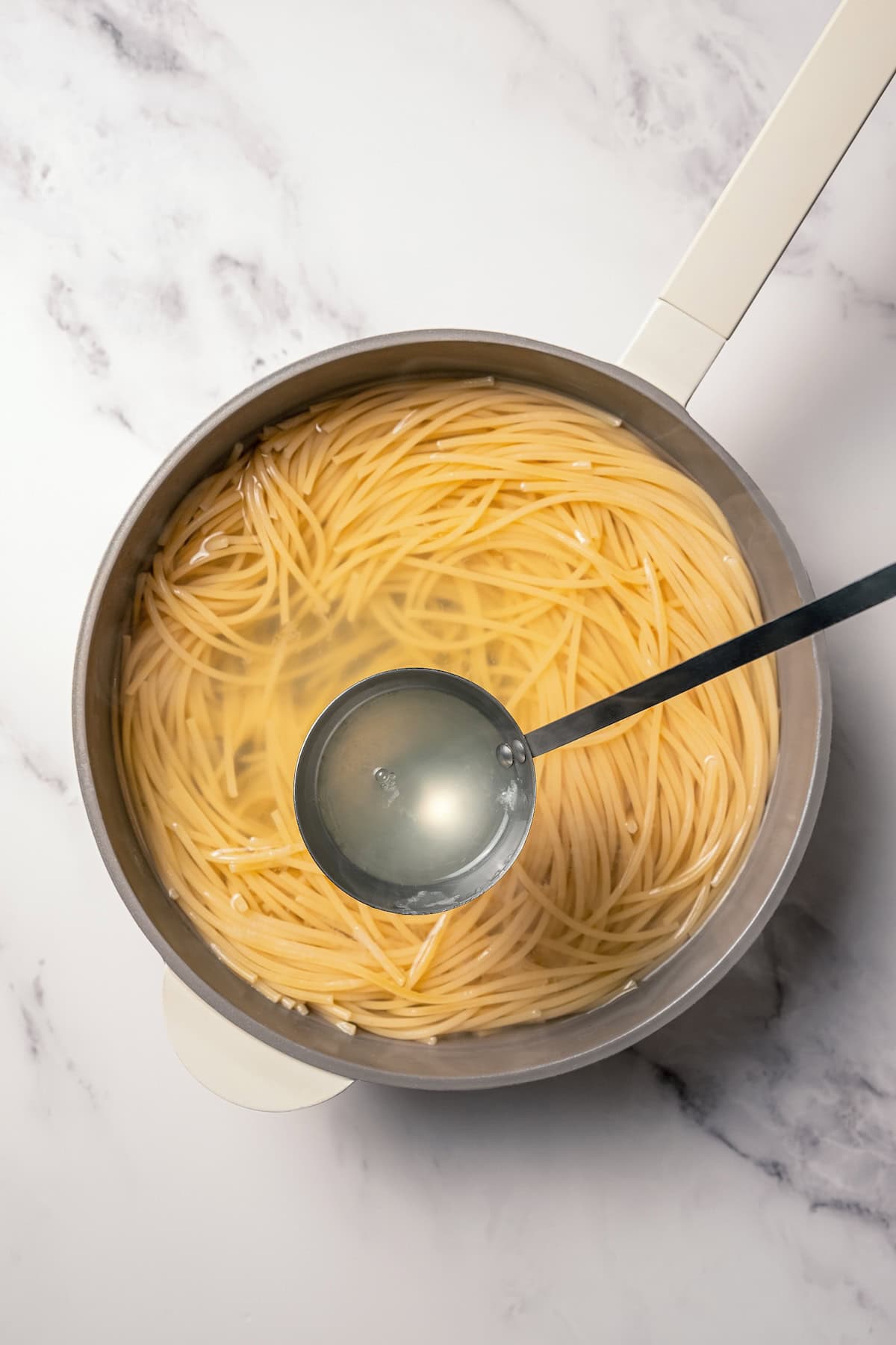 Make saucy garlic butter noodles in 15 minutes! You can adapt this easy recipe with shrimp, chicken, or veggies for a quick weeknight dinner. A ladleful of pasta water held over a pot of cooked spaghetti in starchy water.