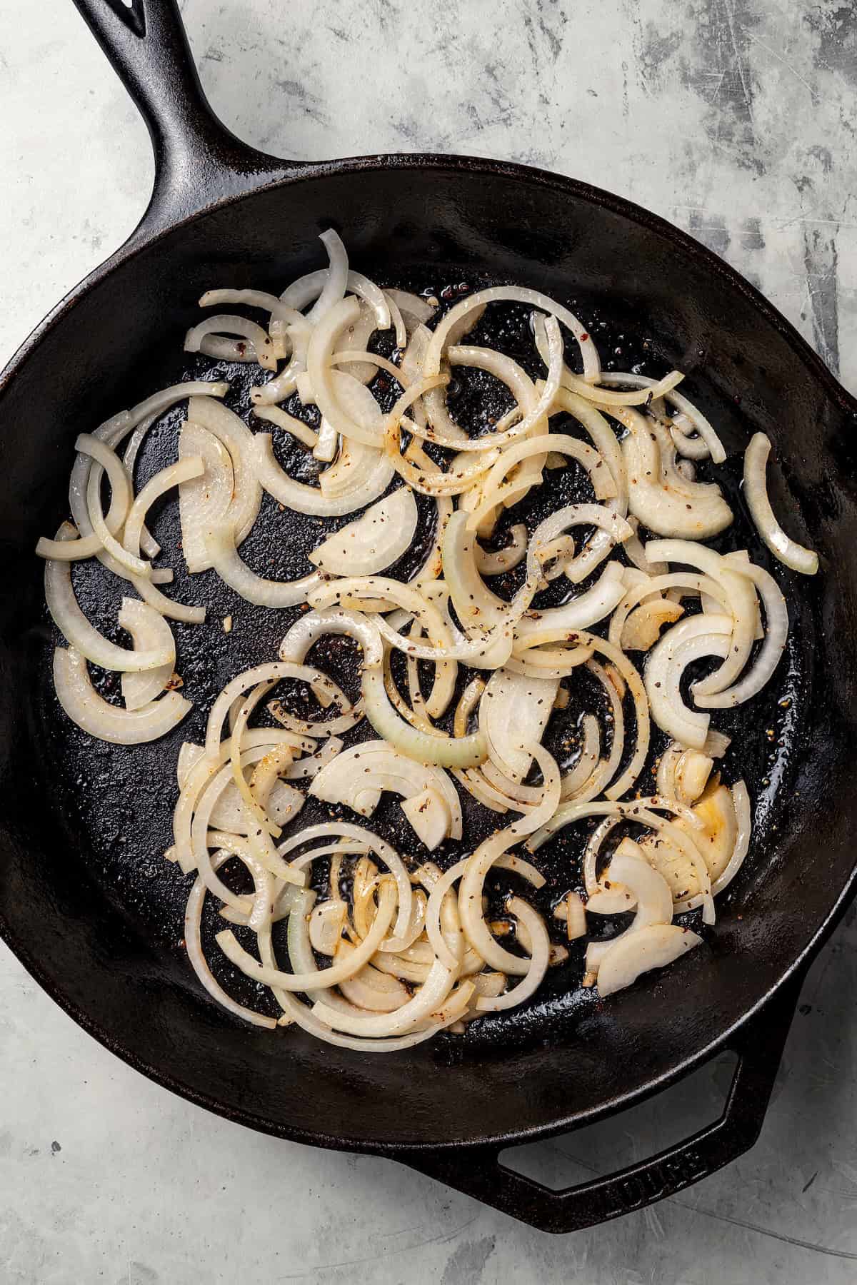 Sliced onions sautéeing in a cast iron skillet.