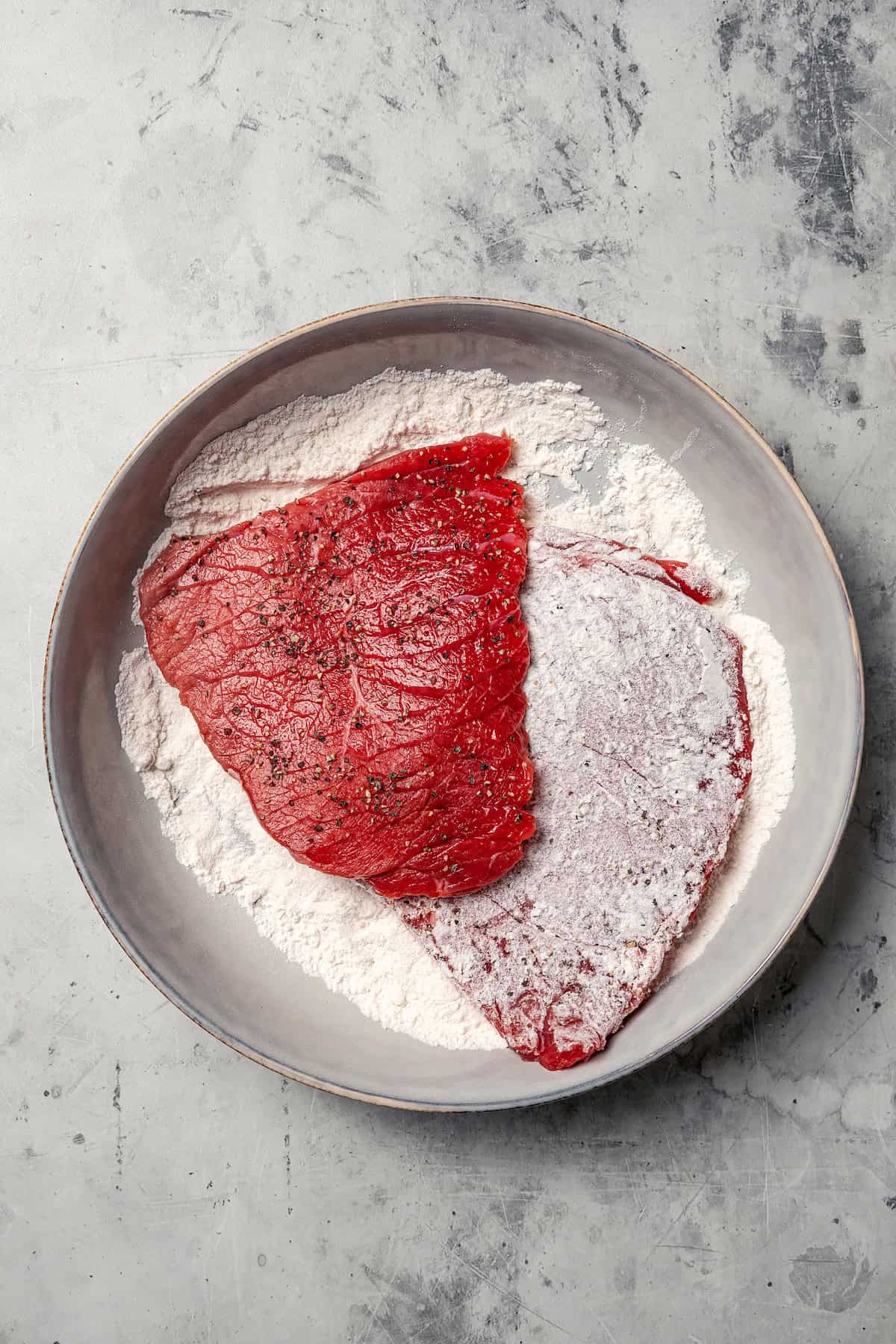 This Swiss steak recipe with gravy is a comforting dinner with juicy beef slow-braised in a rich tomato sauce and served over mashed potatoes. Tenderized steaks partially coated with flour in a shallow dish.