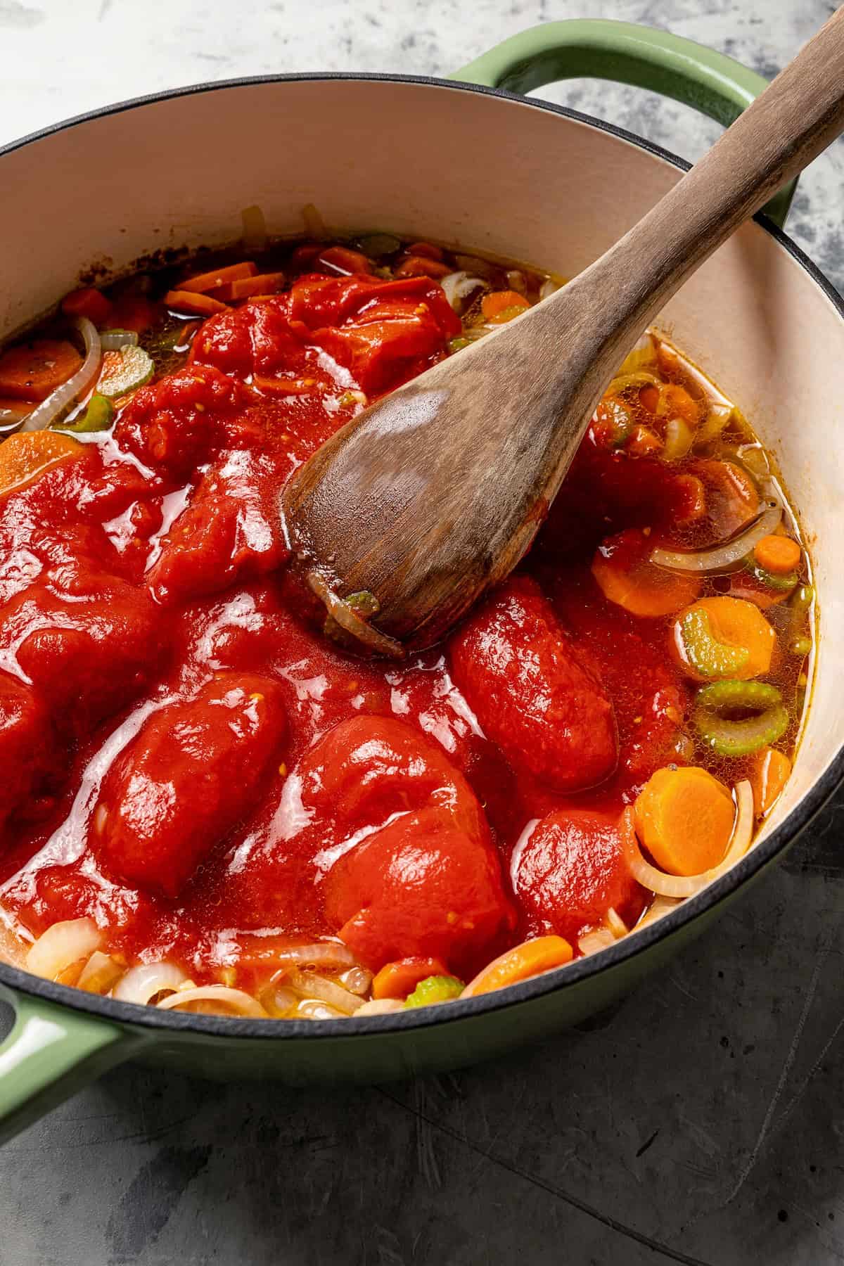 This Swiss steak recipe with gravy is a comforting dinner with juicy beef slow-braised in a rich tomato sauce and served over mashed potatoes. Canned plum tomatoes stirred into a Dutch oven with vegetables and broth using a wooden spoon.
