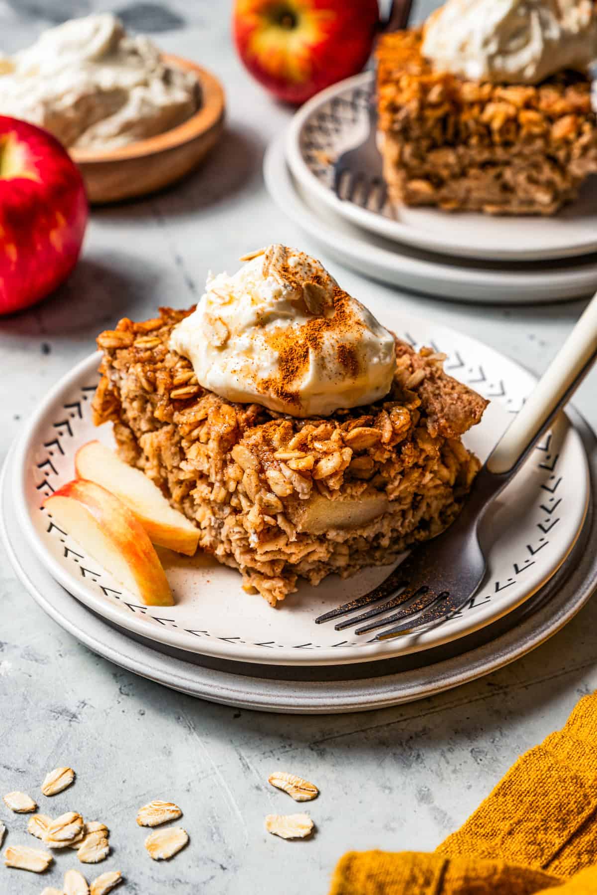 A square of baked apple oatmeal served on a plate and garnished with a dollop of cream.