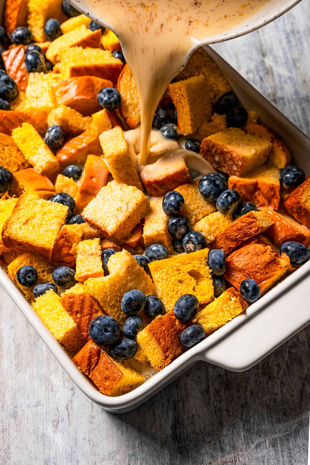 Pouring custard mixture over bread cubes in a baking dish.
