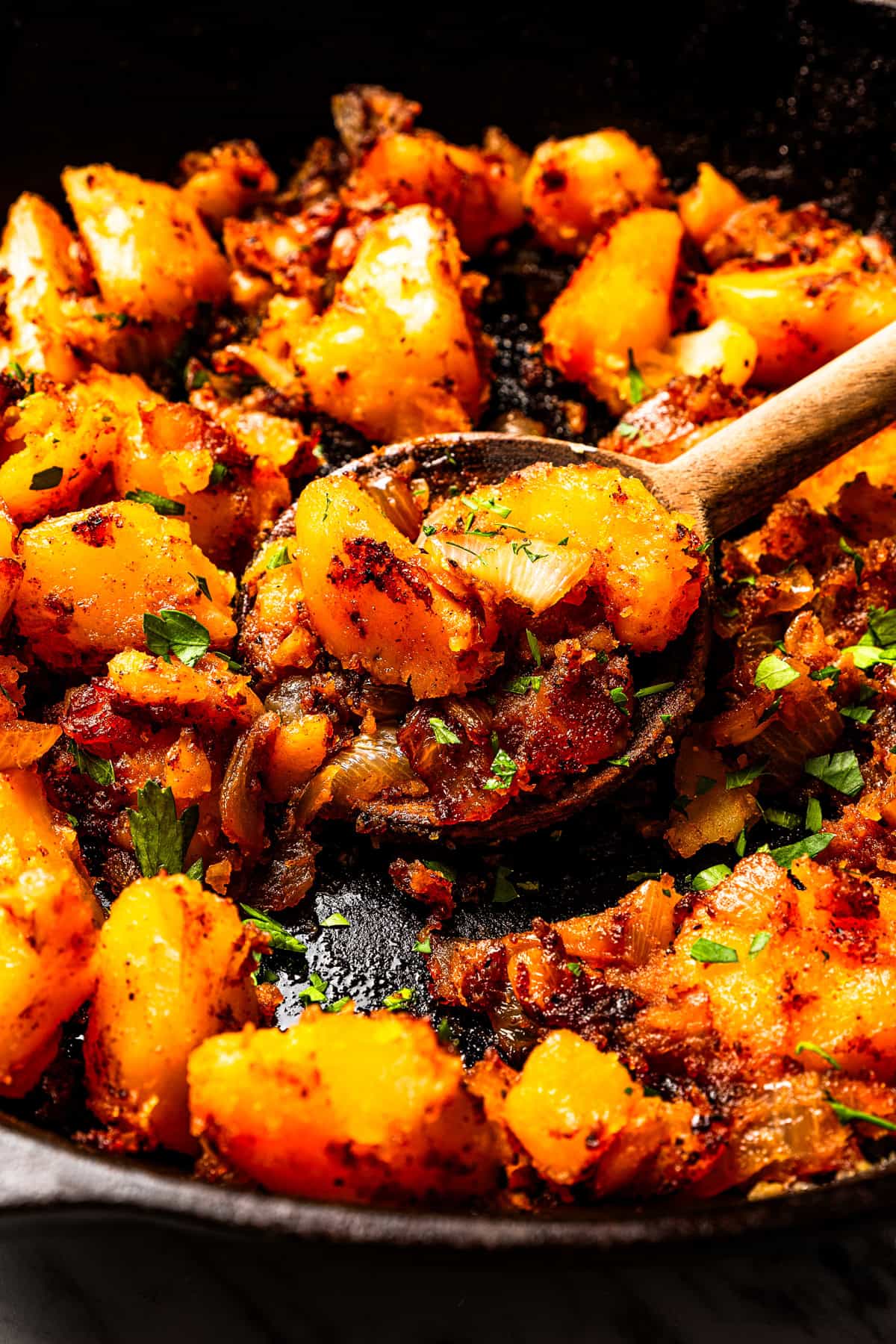 These seasoned and crispy breakfast potatoes are boiled, pan-fried, and finished in the oven so they're fluffy inside with golden-brown edges. A wooden spoon scooping breakfast potatoes in a skillet.