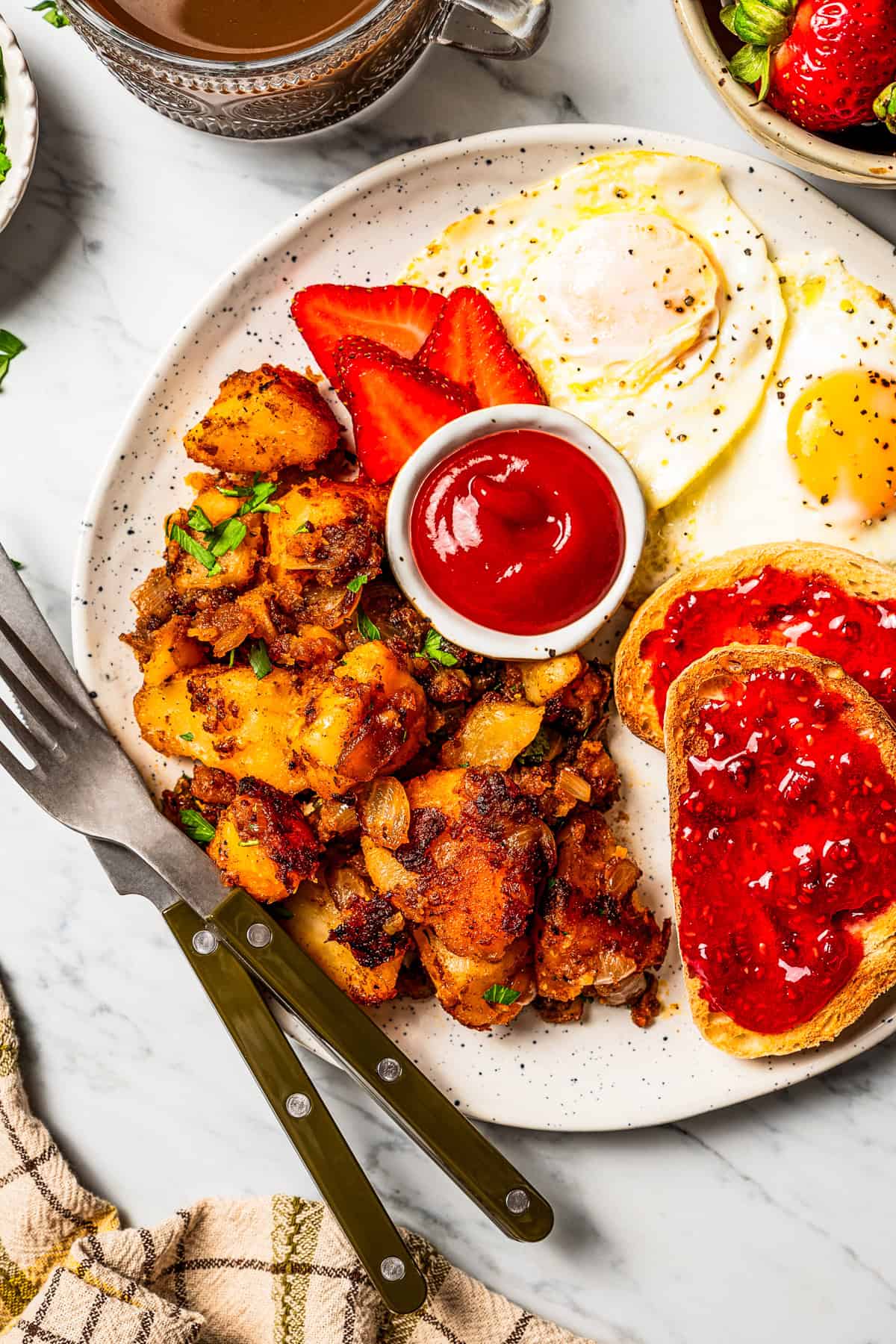 These seasoned and crispy breakfast potatoes are boiled, pan-fried, and finished in the oven so they're fluffy inside with golden-brown edges. A plate of breakfast potatoes served with ketchup next to toast slices with jam, fried eggs, and fresh strawberries.