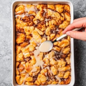 Drizzling icing over a cinnamon roll casserole in a baking dish.