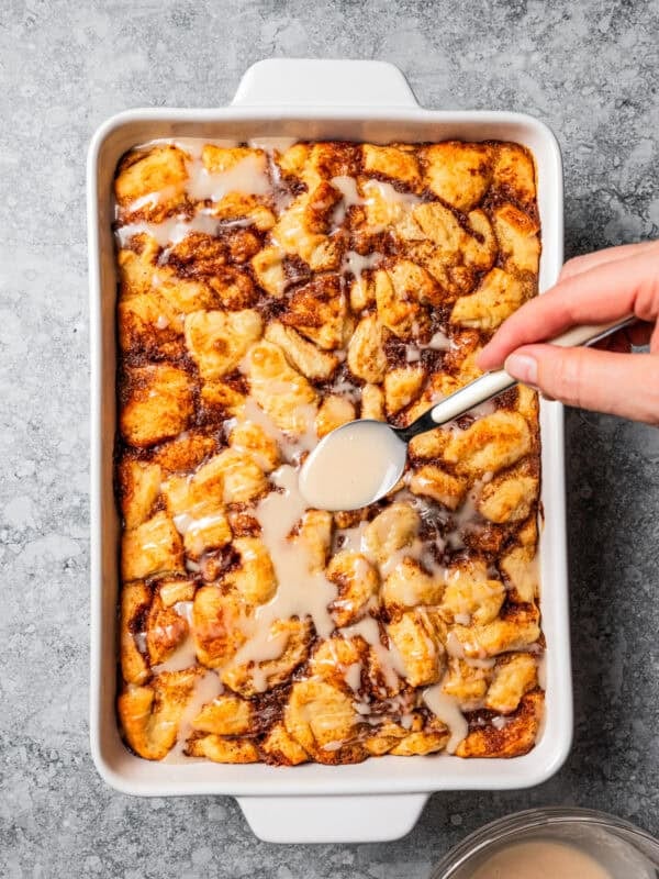 Drizzling icing over a cinnamon roll casserole in a baking dish.