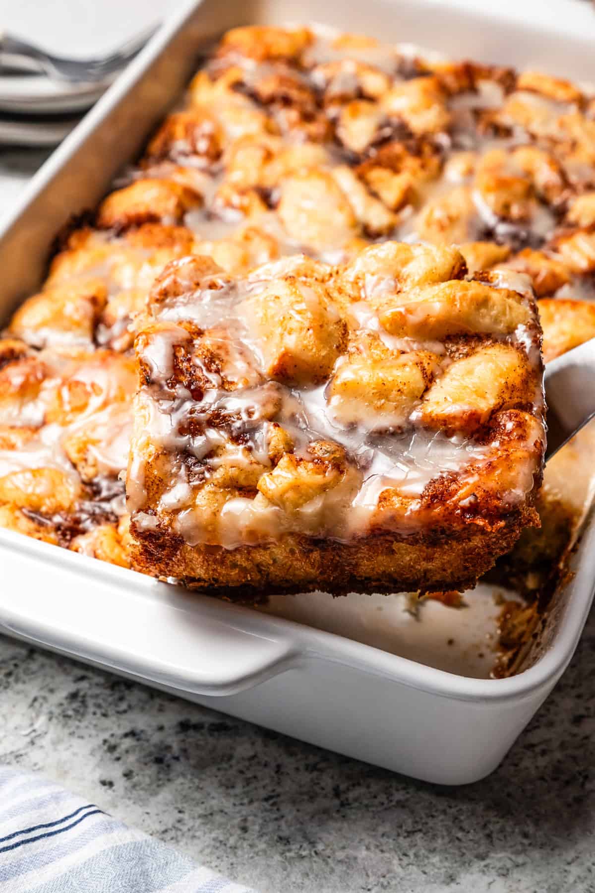 Lifting the corner slice of a cinnamon roll casserole from the baking dish.