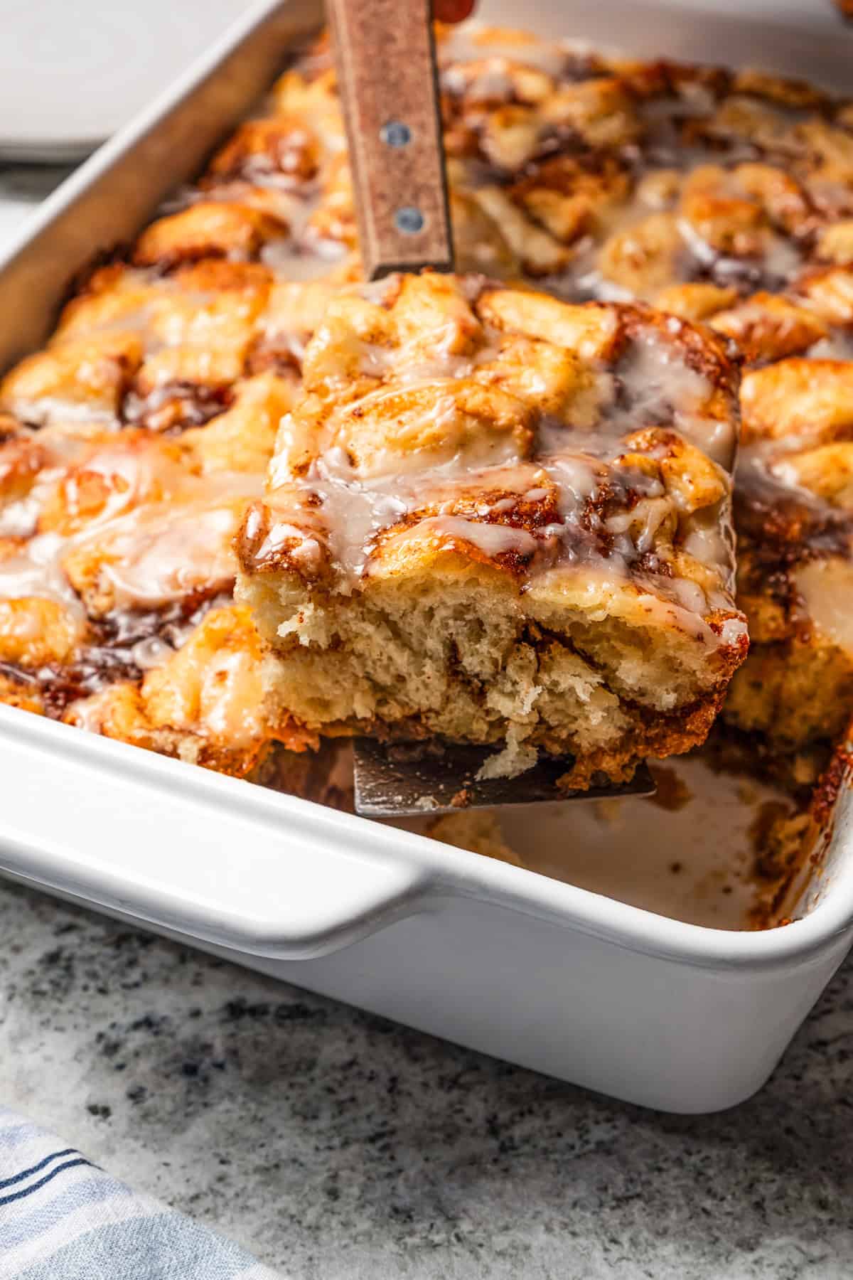 Lifting out a slice of a cinnamon roll casserole from the baking dish.