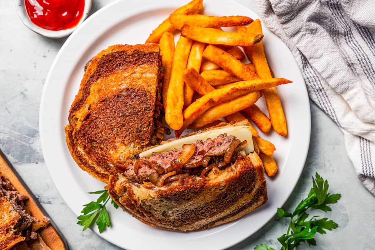 Make the best homemade patty melt recipe with caramelized onions and melty cheese grilled on rye bread. It's easy, diner-style comfort food! Patty melt on a plate with French fries.