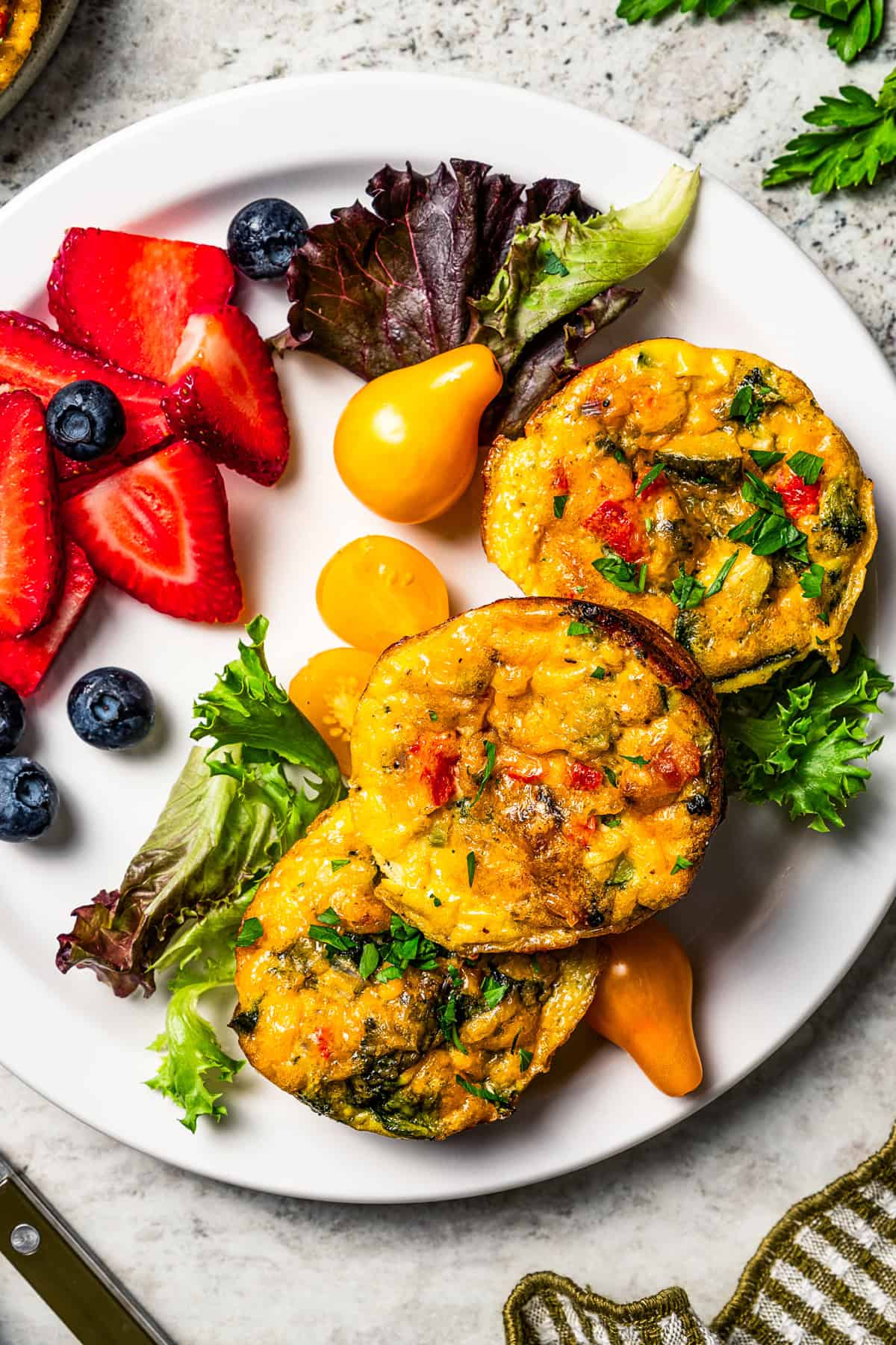Three egg bites stacked on a plate with a side of salad greens and fresh berries.