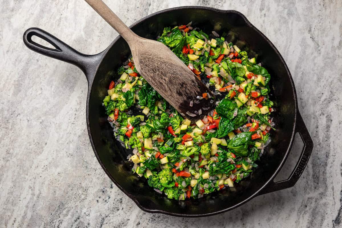 This Starbucks-inspired egg bites recipe with cottage cheese and veggies is quick to bake in a muffin tin. It's an easy, on-the-go breakfast! Sautéed diced vegetables in a skillet with a wooden spoon.