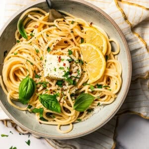 Noodles in a bowl garnished with fresh parsley and lemon wedges.