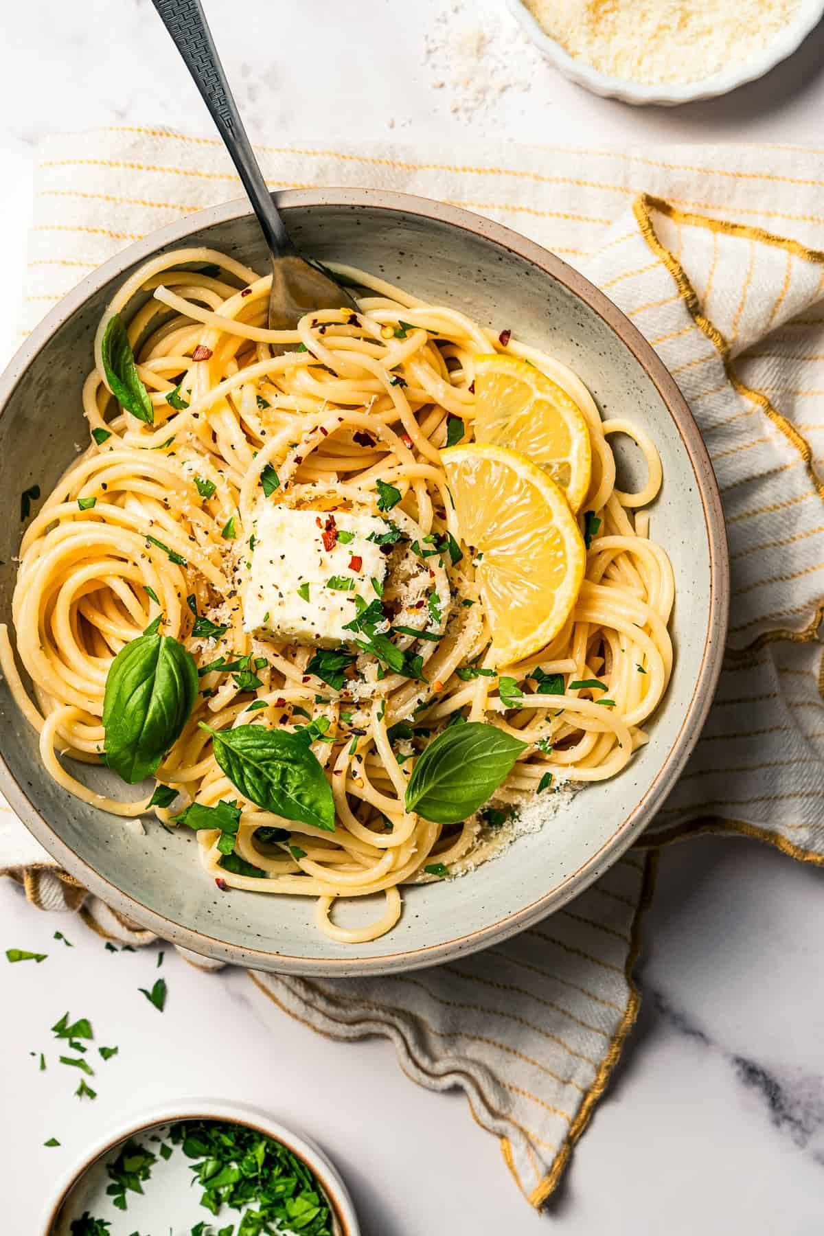Noodles in a bowl garnished with fresh parsley and lemon wedges.