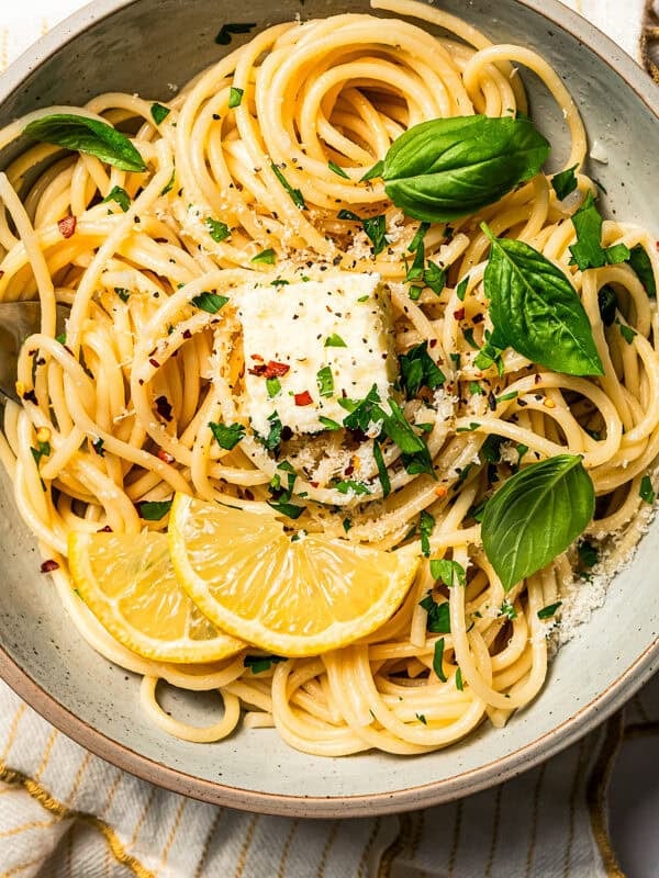 Noodles in a bowl garnished with fresh parsley and lemon wedges.