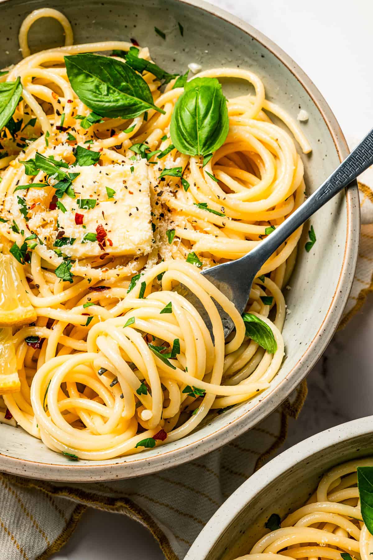 A fork twirling noodles in a bowl, garnished with fresh parsley and lemon wedges.