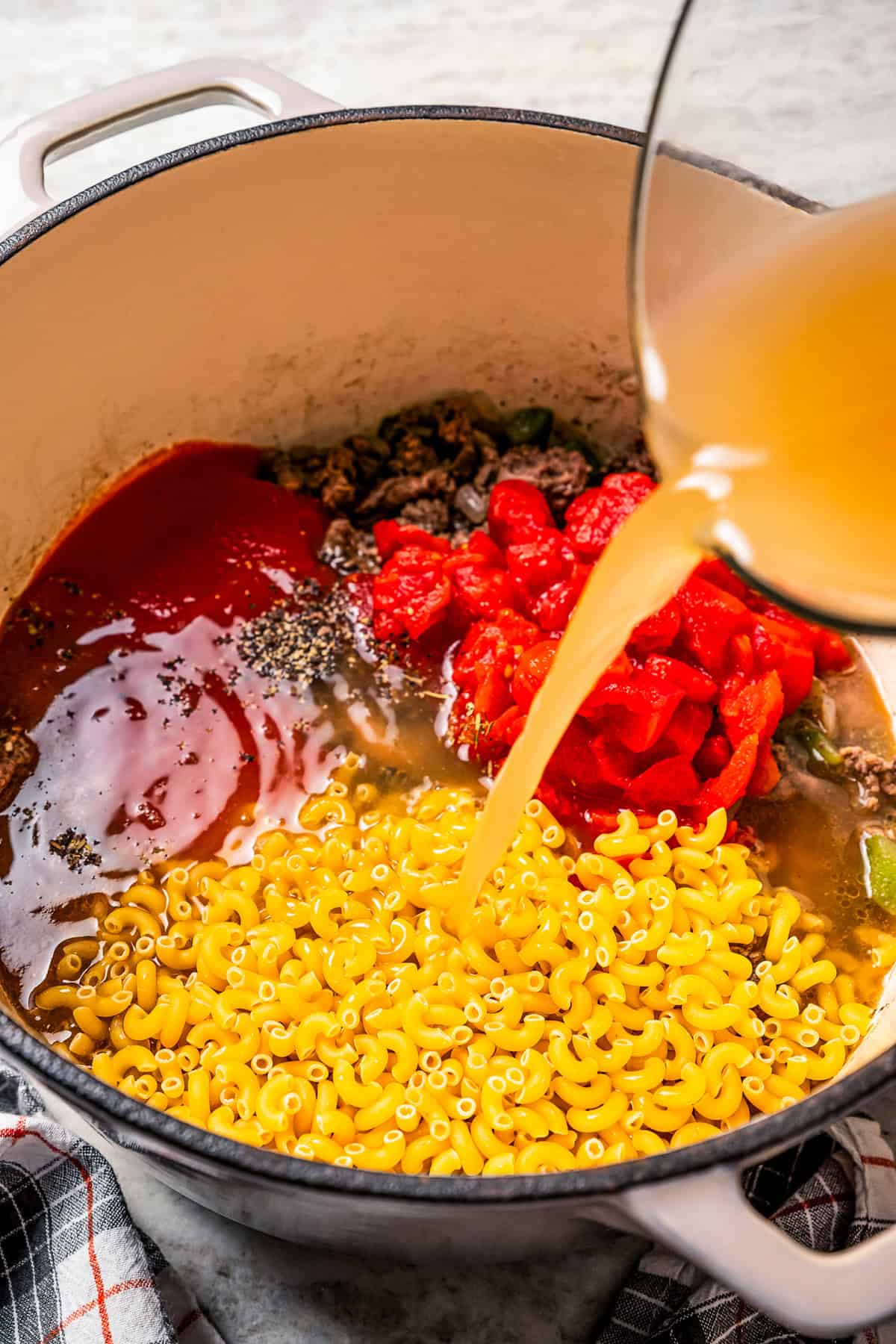 Pasta, tomatoes, and broth added to a pot with ground beef, onions, and peppers.