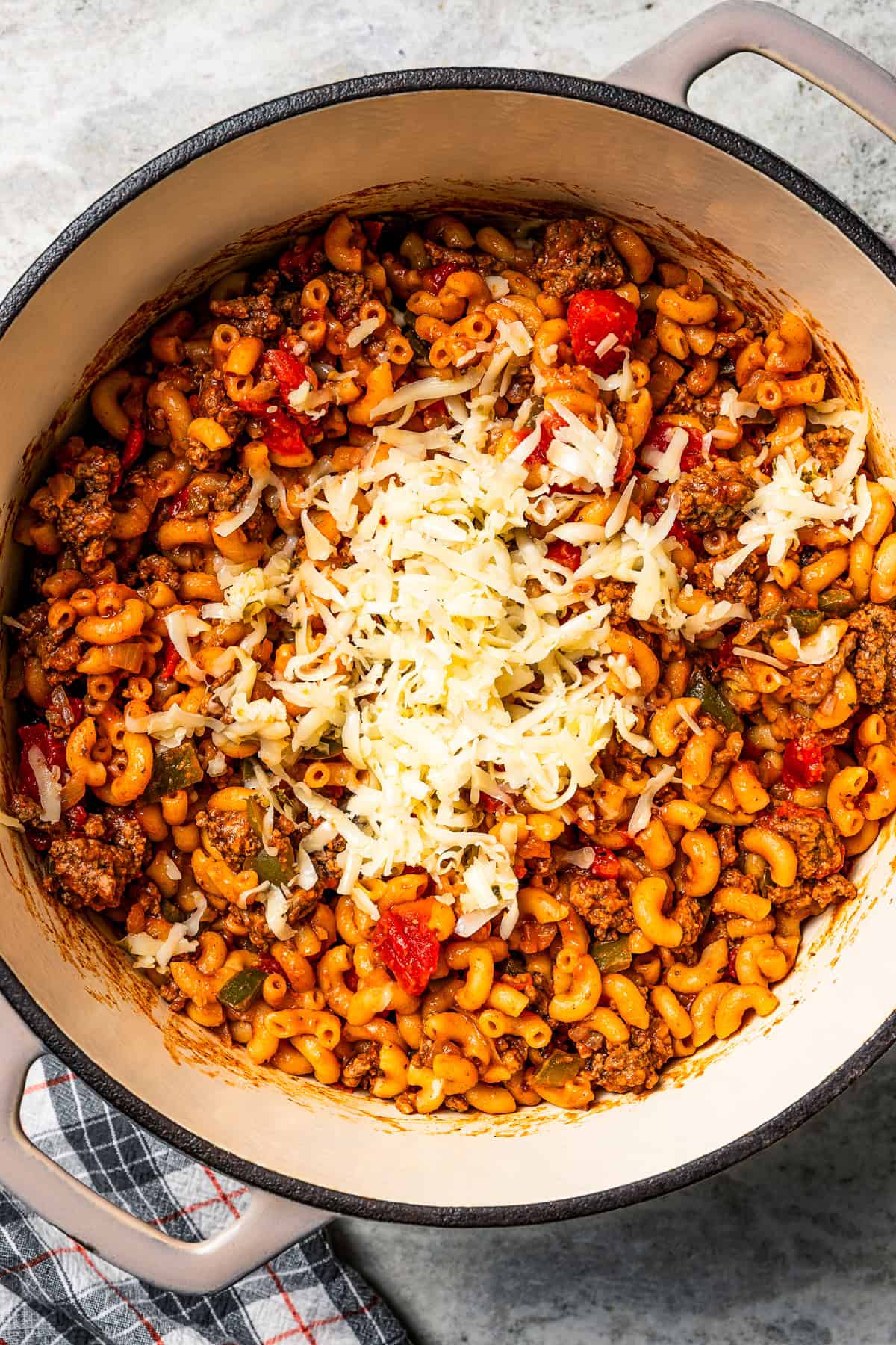 Shredded cheese sprinkled over cooked goulash in a pot.