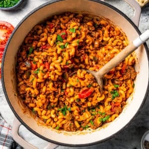 Goulash in a pot with a wooden spoon stirring through it.
