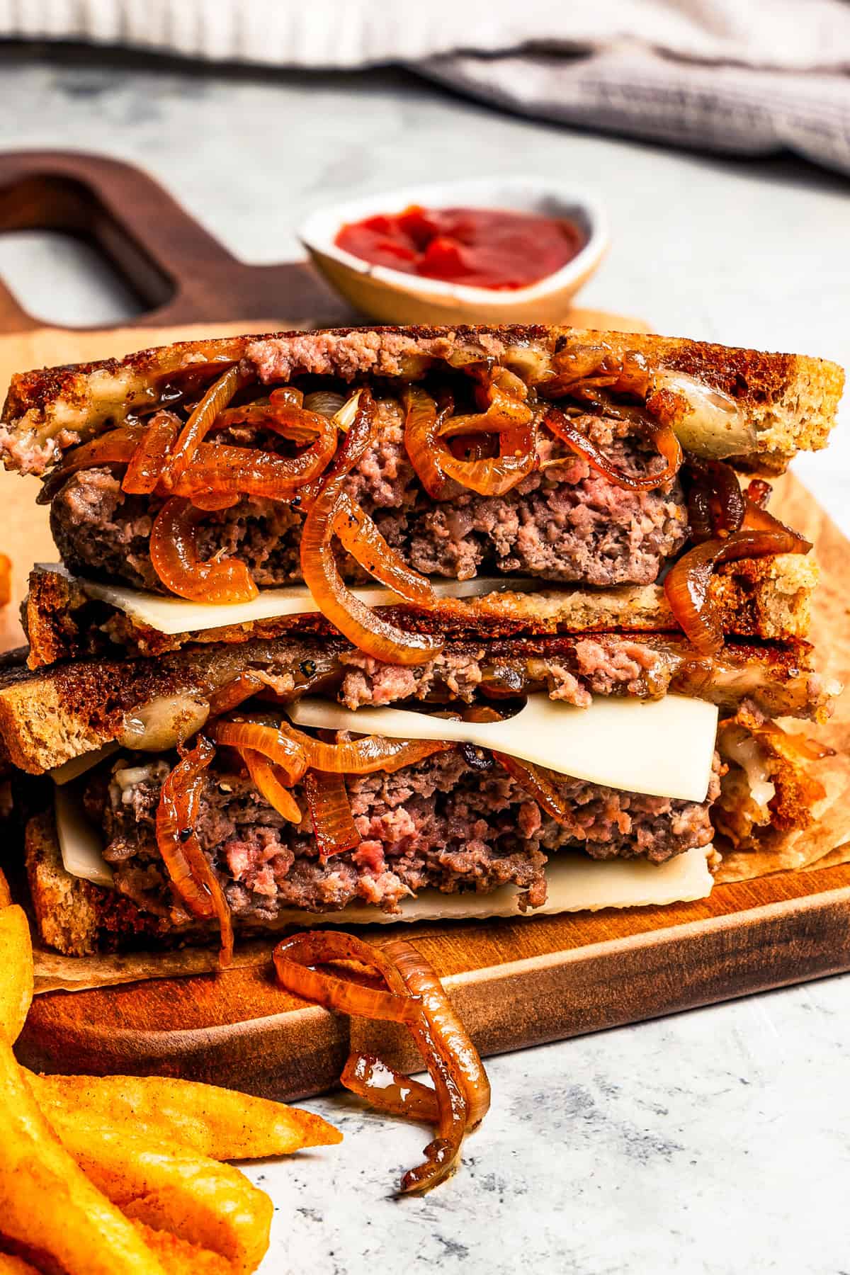 Two halves of a patty melt with cheese and caramelized onions stacked on a wooden cutting board.
