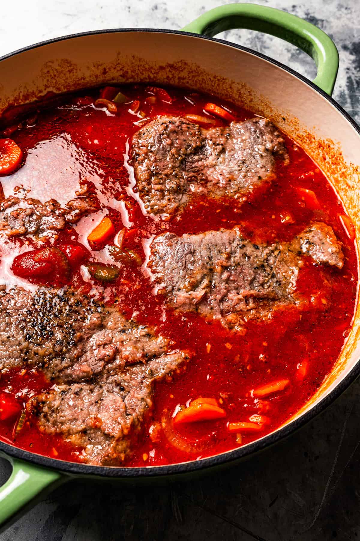 This Swiss steak recipe with gravy is a comforting dinner with juicy beef slow-braised in a rich tomato sauce and served over mashed potatoes. Four steaks are cooking in tomato sauce.