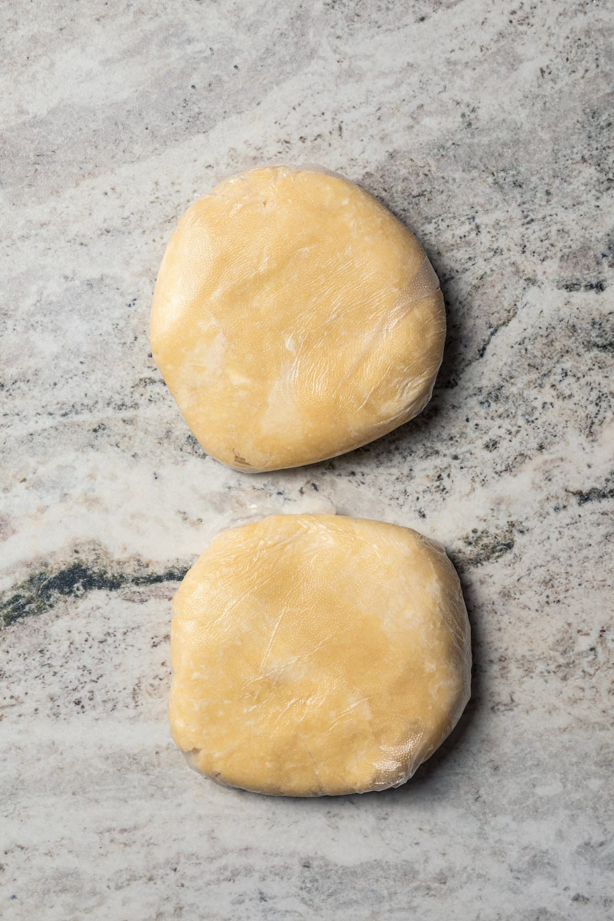 This easy beef pot pie recipe has a hearty, savory filling of juicy braised beef and tender veggies baked inside a flaky homemade pie crust. Two discs of homemade pie dough on a countertop.