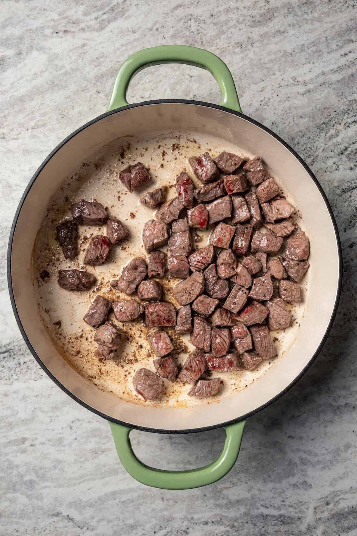 This easy beef pot pie recipe has a hearty, savory filling of juicy braised beef and tender veggies baked inside a flaky homemade pie crust. Browned beef cubes in a skillet.