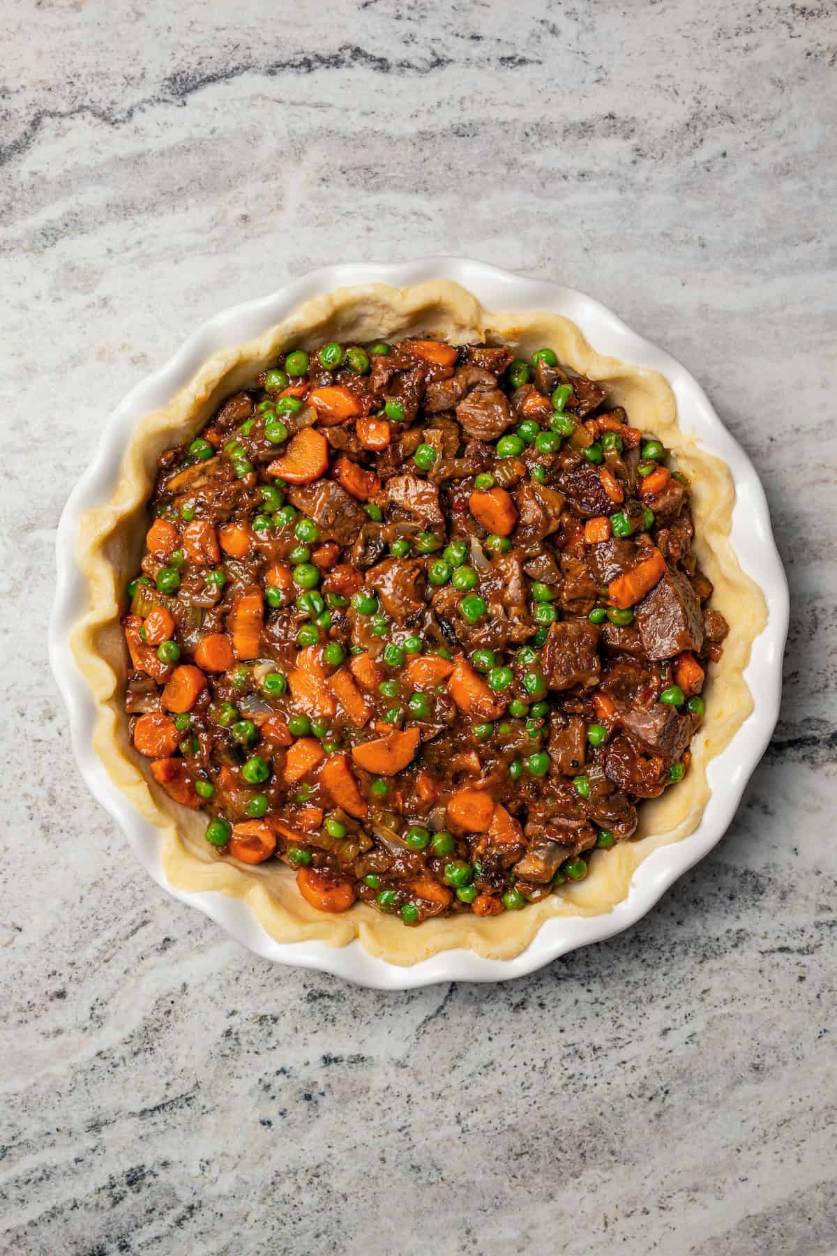 This easy beef pot pie recipe has a hearty, savory filling of juicy braised beef and tender veggies baked inside a flaky homemade pie crust. Homemade pie crust in a pie plate filled with beef and vegetable filling.