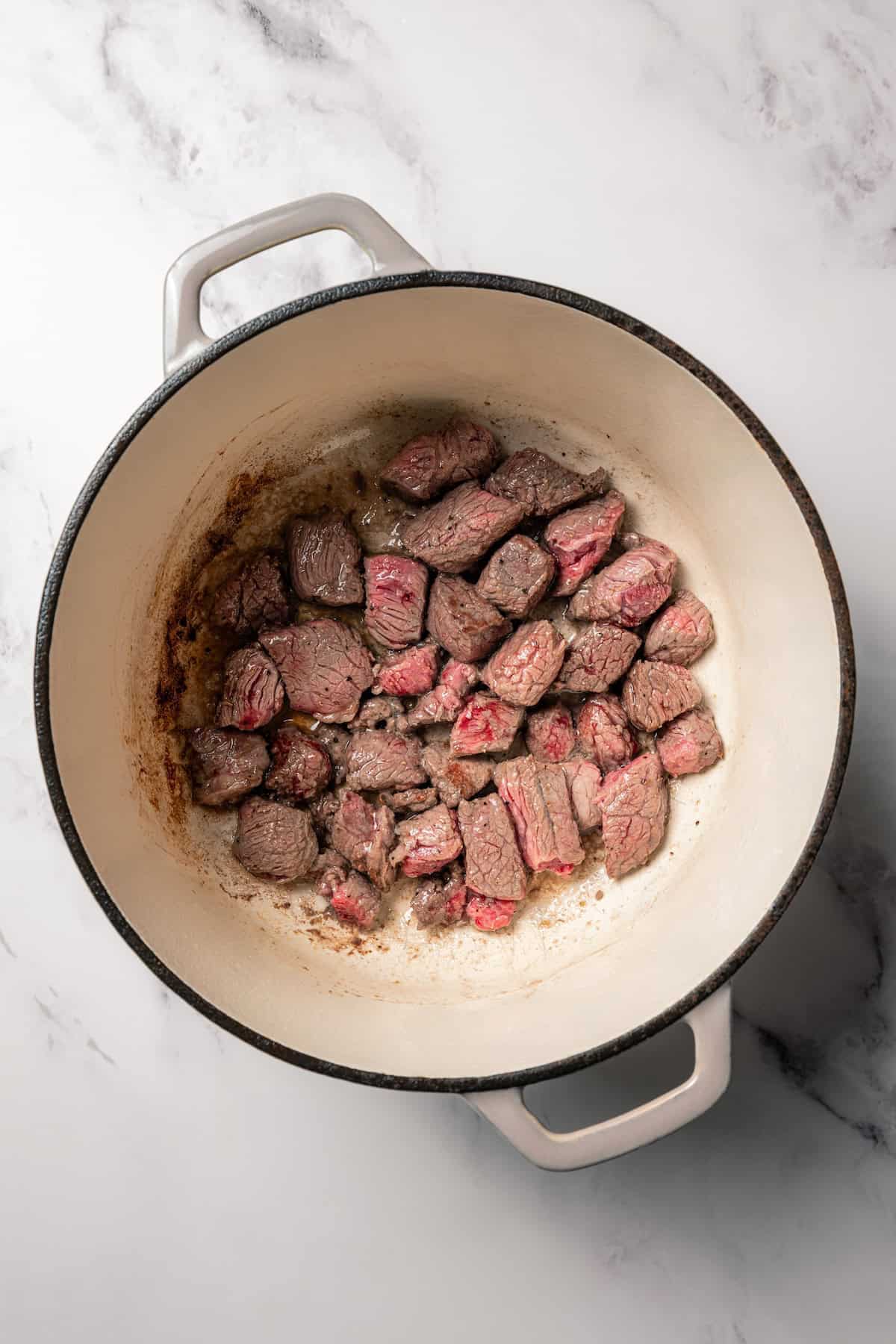 Carne guisada is a flavorful Latin stew with juicy beef slow-cooked in gravy with tomatoes, jalapeños, and spices. Make it at home in one pot! Browned beef chunks in a large pot.