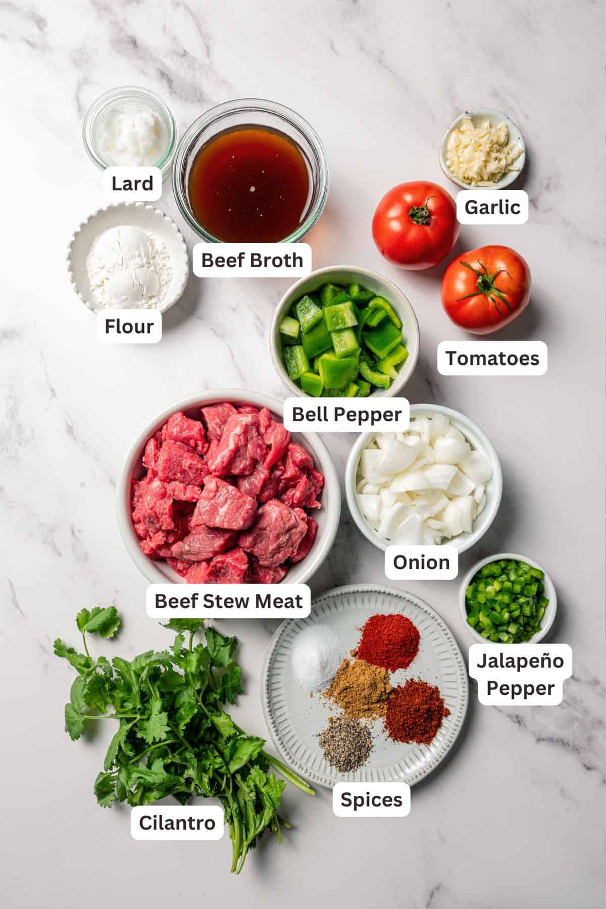 Carne guisada is a flavorful Latin stew with juicy beef slow-cooked in gravy with tomatoes, jalapeños, and spices. Make it at home in one pot! Carne guisada ingredients with text labels overlaying each ingredient.