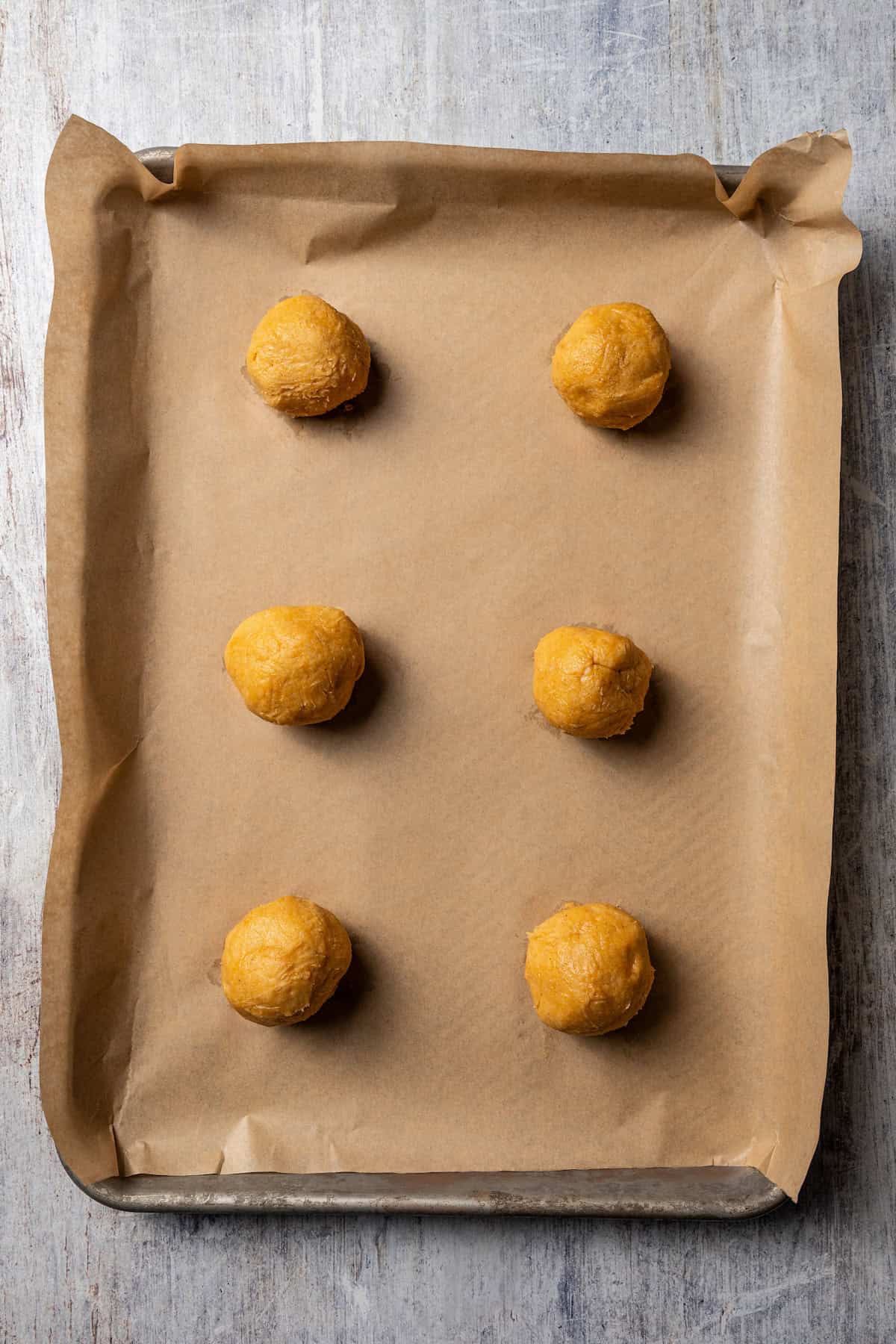 These easy, soft-baked sweet potato cookies are made with sweet potato purée, fall spices, and stuffed with sweet cream cheese in the middle! Overhead view of sweet potato cookie dough balls stuffed with cream cheese on a baking sheet lined with parchment paper.