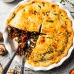 Beef pot pie served in a pie plate with a slice removed from it to expose the meat filling.