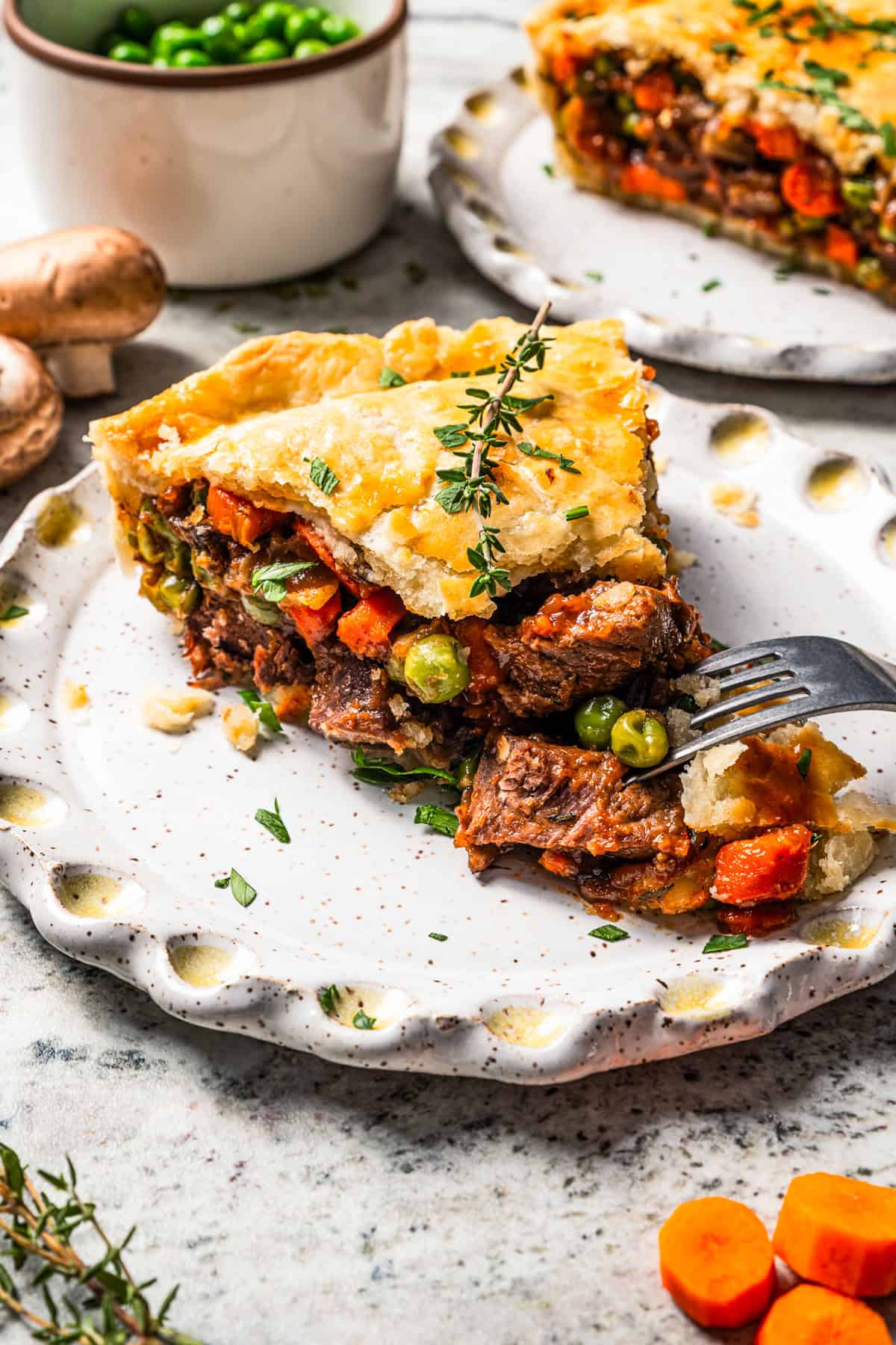 This easy beef pot pie recipe has a hearty, savory filling of juicy braised beef and tender veggies baked inside a flaky homemade pie crust. A fork cutting into a slice of homemade beef pot pie garnished with thyme sprigs on a plate.