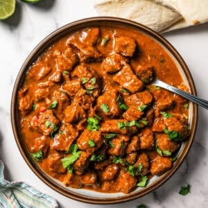 Overhead view of carne guisada in a large bowl with a spoon, next to tortillas and a lime sliced in half.
