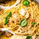 Overhead view of chicken carbonara in a pot with two serving tongs.