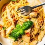 A fork stirring through chicken and spaghetti from a bowl of carbonara.