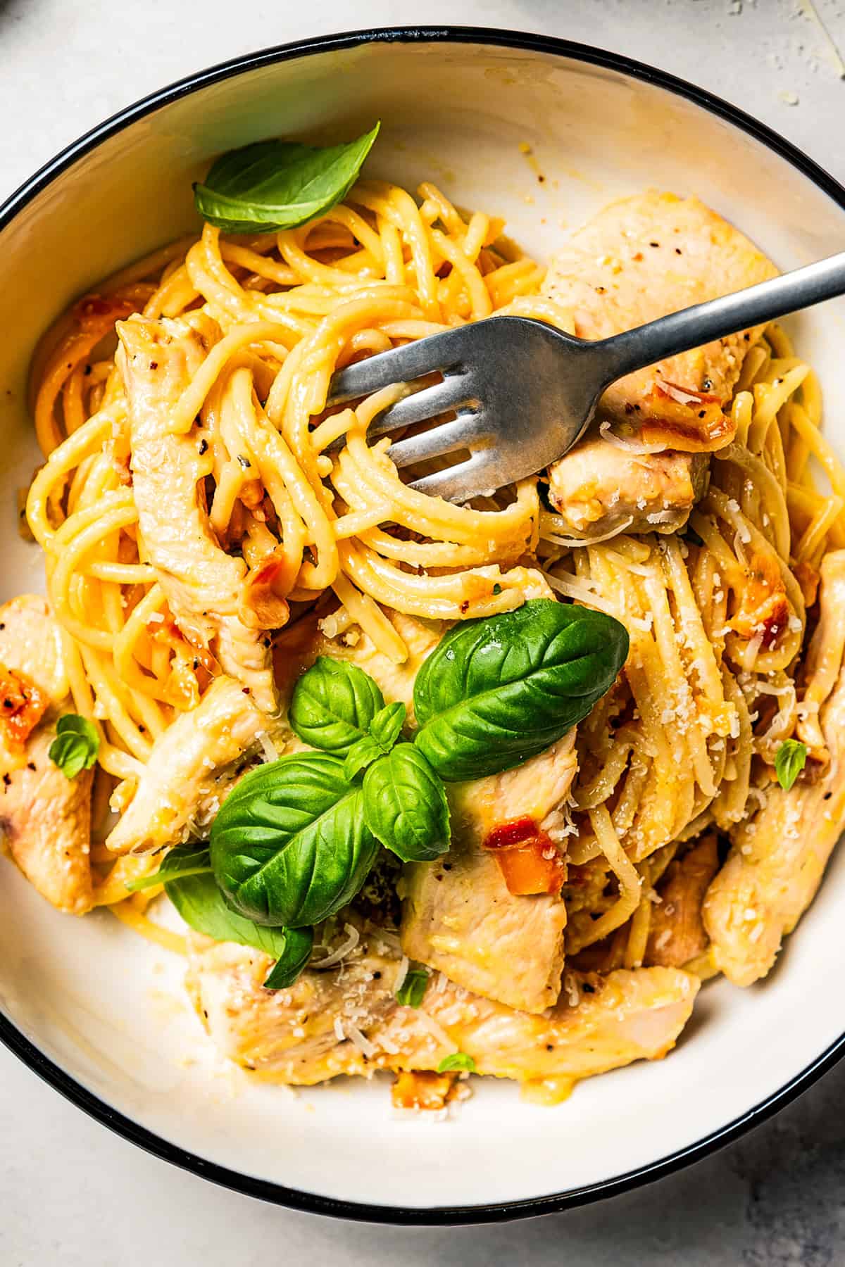 Make the best chicken carbonara in 30 minutes! This is a creamy pasta with parmesan, pancetta, and tender chicken, perfect for weeknights. A fork stirring through chicken and spaghetti from a bowl of carbonara.