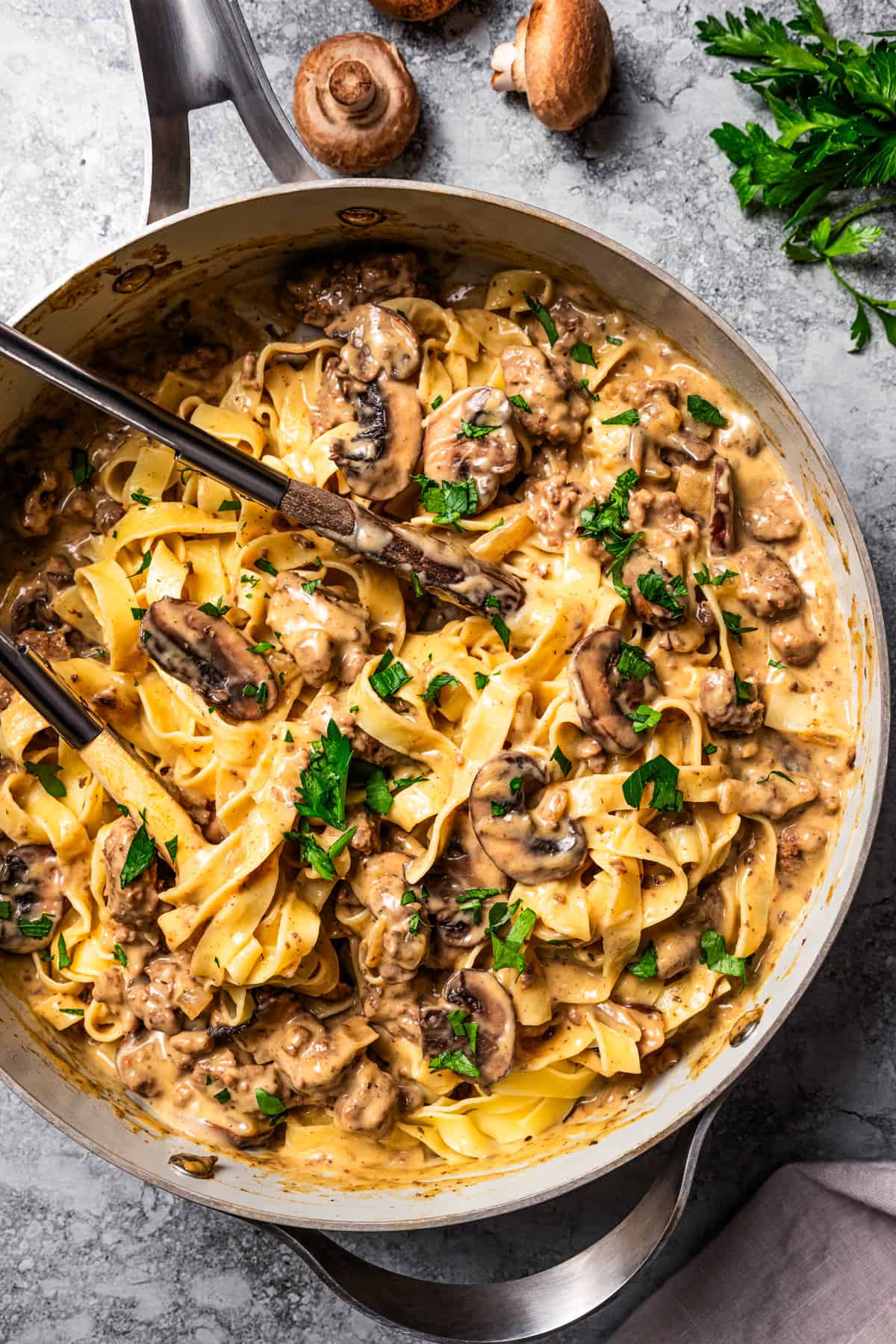 A wooden spoon stirring hamburger stroganoff in a skillet.