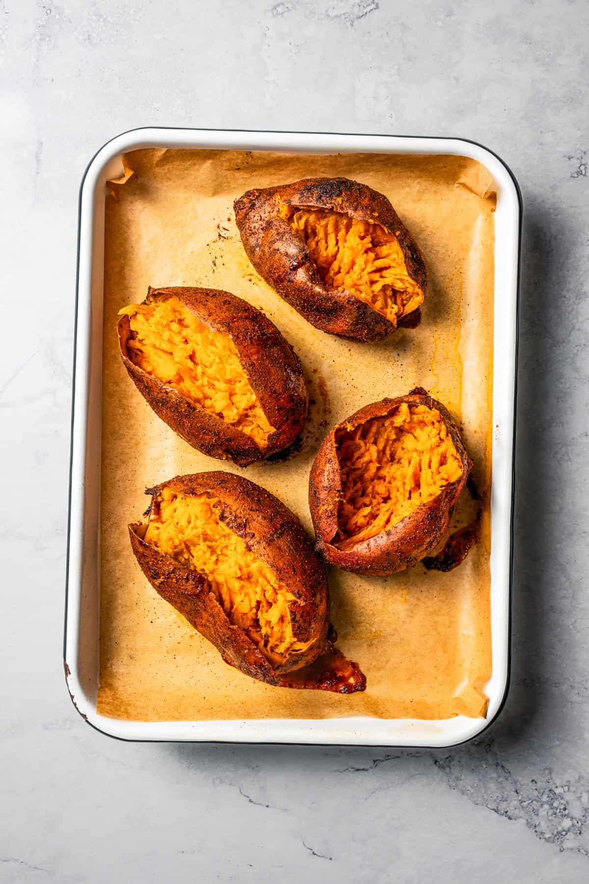 Four baked sweet potatoes are split open and arranged in a baking pan.