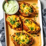 Four Southwest stuffed sweet potatoes next to a small bowl of homemade avocado crema on a rimmed baking pan.
