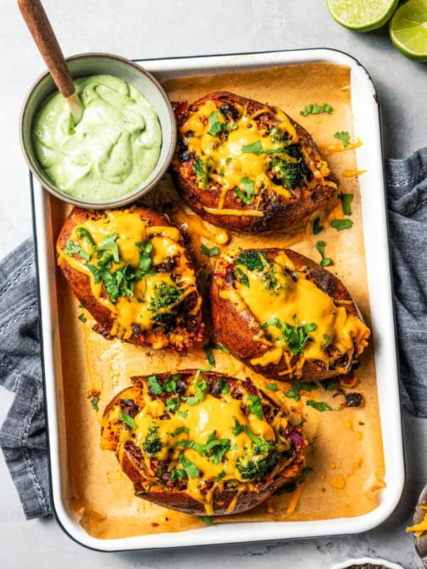 Four Southwest stuffed sweet potatoes next to a small bowl of homemade avocado crema on a rimmed baking pan.