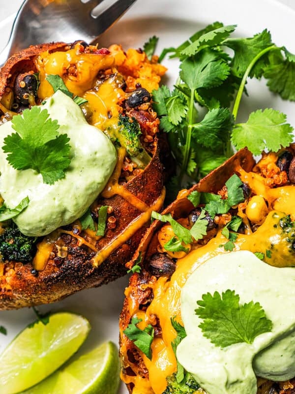 Two southwest stuffed sweet potatoes topped with avocado crema and served on a plate.