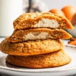 Sweet potato cookies stacked on a plate, with the top cookie cut in half to show the sweet cream cheese filling.