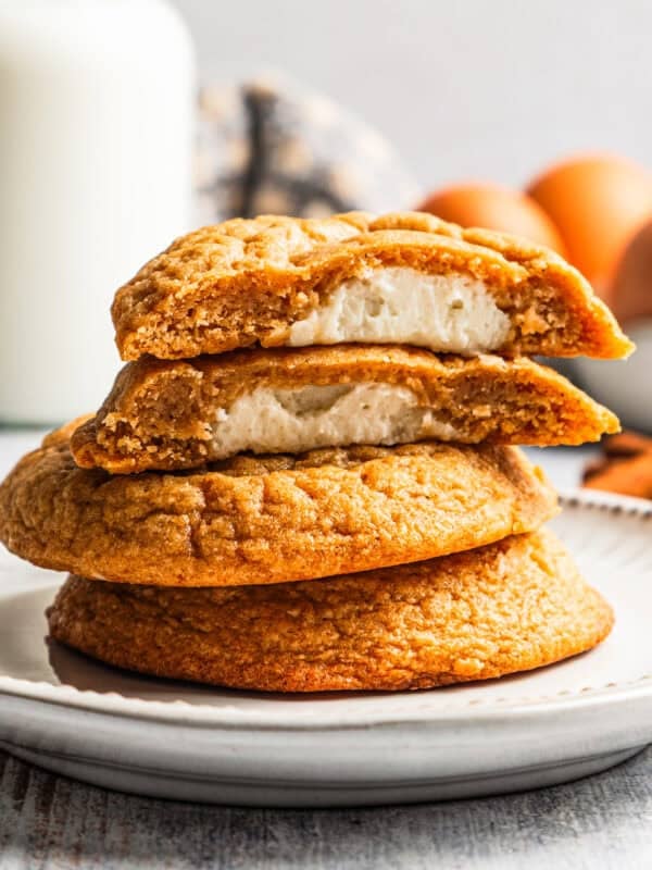 Sweet potato cookies stacked on a plate, with the top cookie cut in half to show the sweet cream cheese filling.