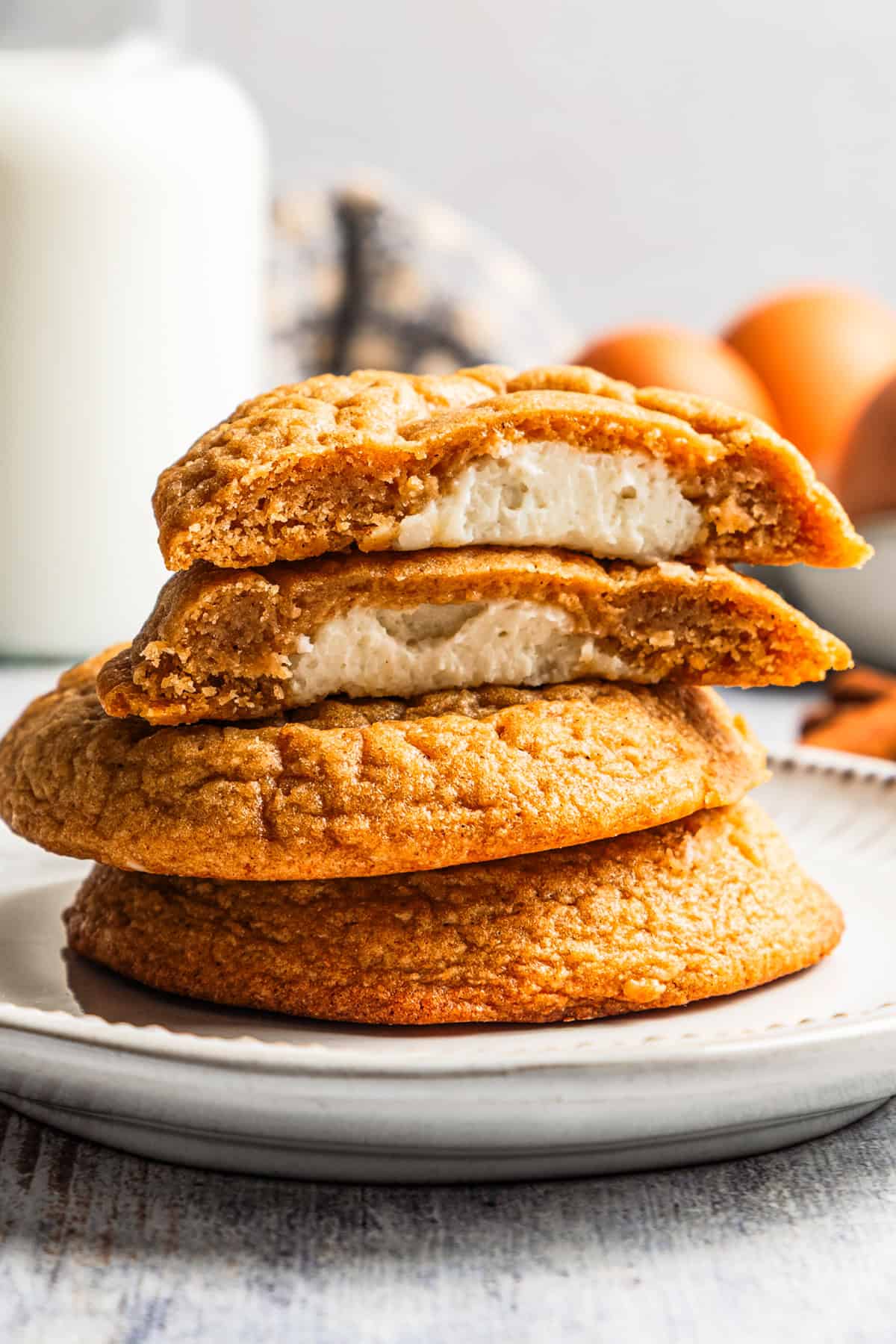 These easy, soft-baked sweet potato cookies are made with sweet potato purée, fall spices, and stuffed with sweet cream cheese in the middle! Sweet potato cookies stacked on a plate, with the top cookie cut in half to show the sweet cream cheese filling.