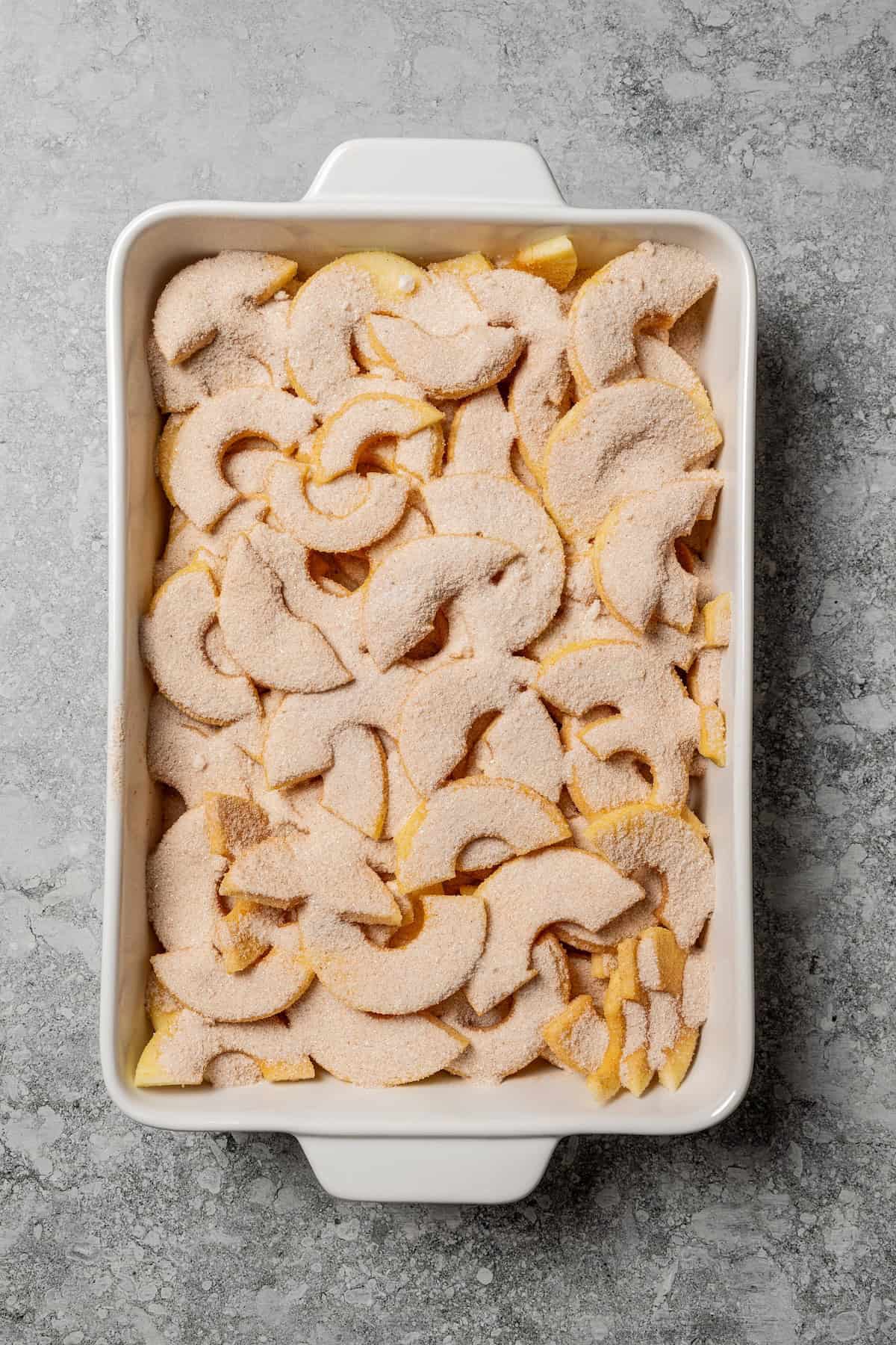 This old-fashioned apple crisp is a classic dessert, with apples, real apple cider, and warm spices baked under a light, crispy oat topping. Sliced apples topped with cinnamon sugar mixture in a baking pan.