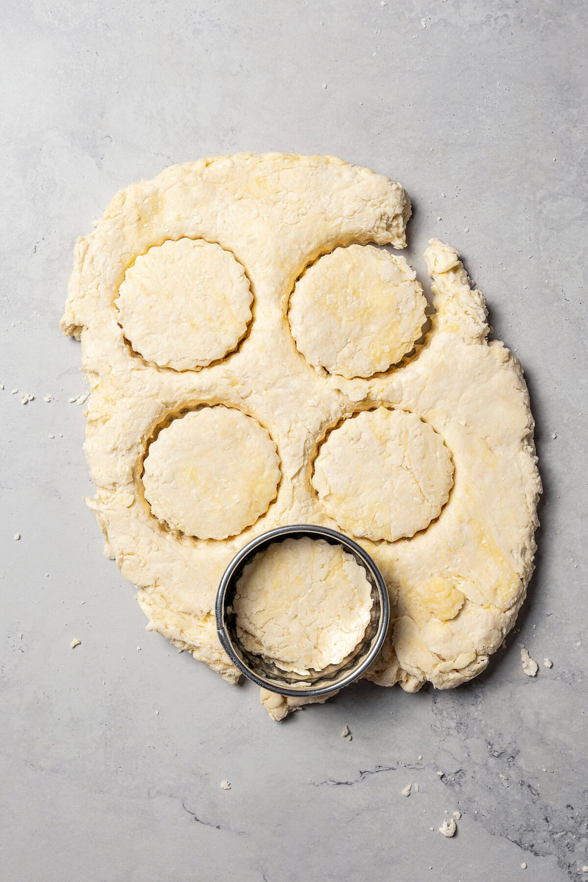 A round biscuit cutter cutting out biscuit dough.