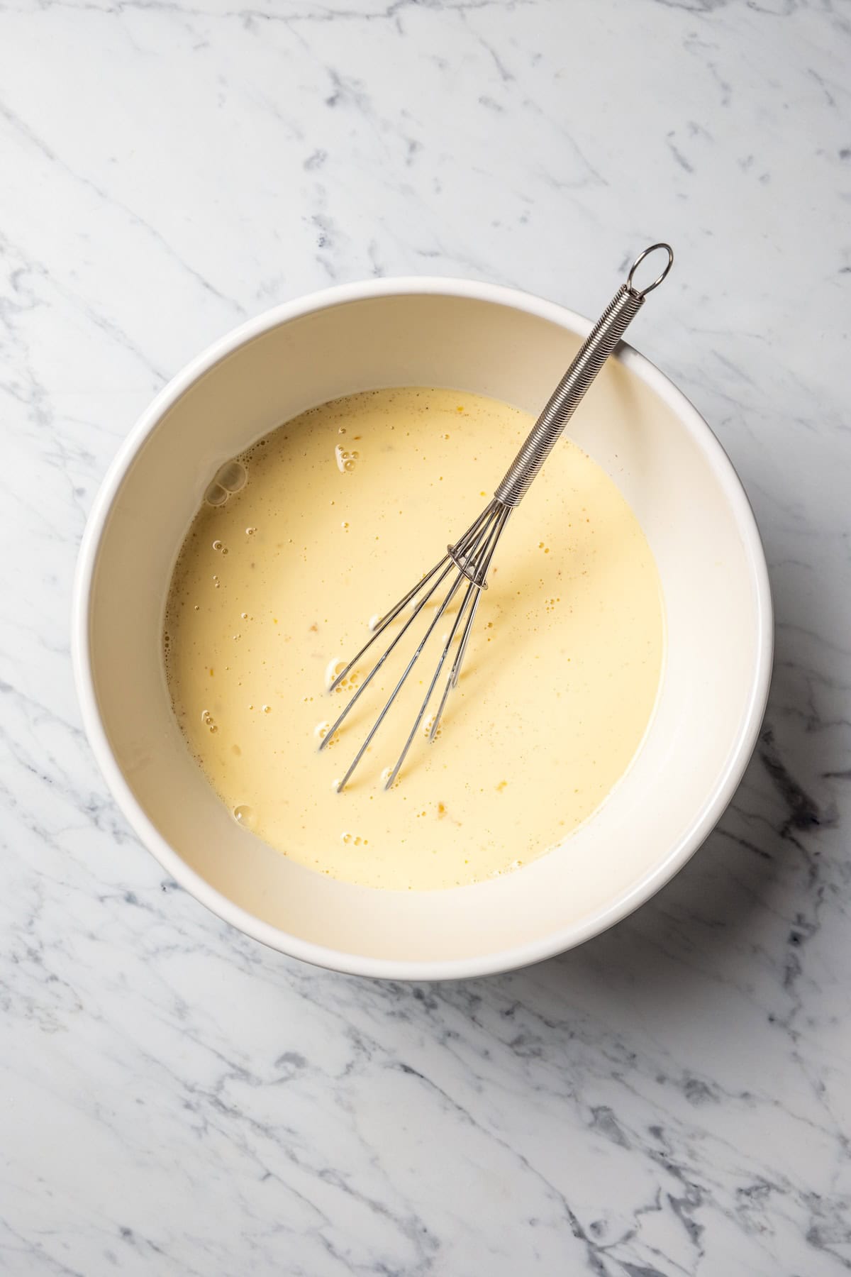 Make thick, fluffy challah bread French toast soaked in an eggy custard with cinnamon, vanilla, and grated nutmeg. The best weekend breakfast! A whisk resting in a bowl of custard.