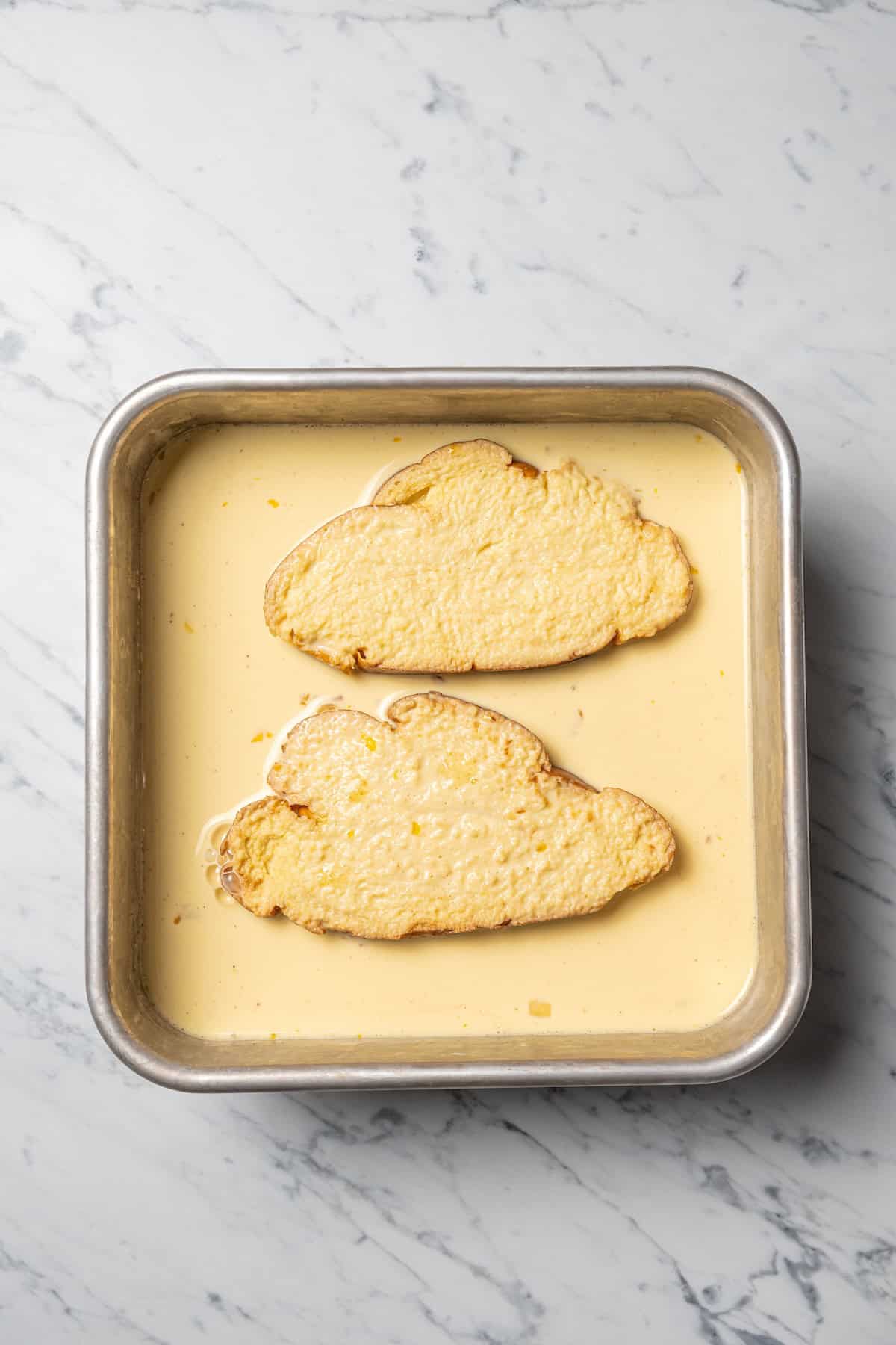 Make thick, fluffy challah bread French toast soaked in an eggy custard with cinnamon, vanilla, and grated nutmeg. The best weekend breakfast! Two slices of challah bread soaking in a pan of custard for French toast.