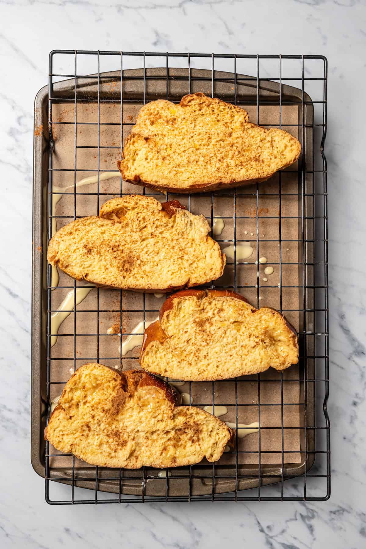 Make thick, fluffy challah bread French toast soaked in an eggy custard with cinnamon, vanilla, and grated nutmeg. The best weekend breakfast! Challah bread slices soaked in custard on a wire rack set over a baking sheet.