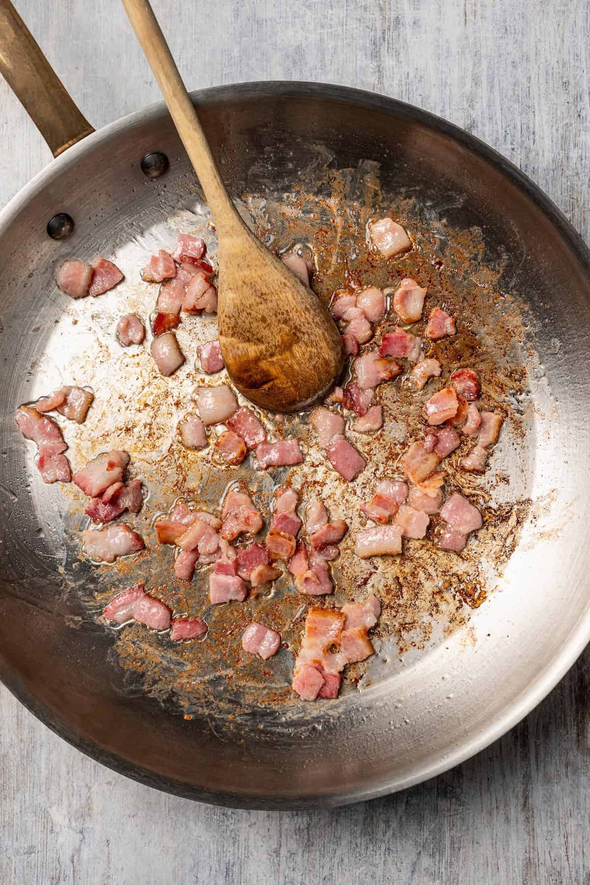 This chicken and bacon pasta is a 20-minute meal with tender linguine, juicy chicken, bacon, and parmesan in a creamy, Carbonara-style sauce. Bacon cooking in a skillet.
